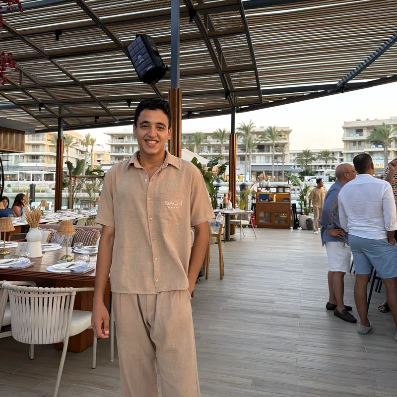 Sachi Marassi server in a beige linen shirt and trousers on the restaurant terrace