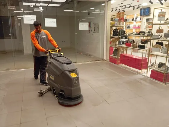 SIAC cleaner in an orange and grey top driving a floor scrubber in a mall
