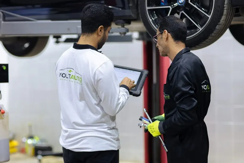 Volt Auto technicians in white and black uniforms working under a car with a tablet